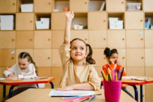 child raising hand in classroom, selling your preschool